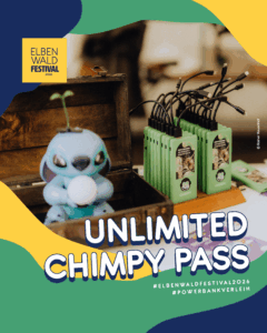 Ein farbenfrohes Bild vom Elbenwald Festival 2026, das einen "Unlimited Chimpy Pass" zeigt. Im Vordergrund steht eine Spielfigur und im Hintergrund sind grüne Powerbanks zur Ausleihe auf einem Tisch zu sehen.