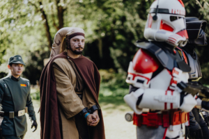 501st Legion Teilnehmer in Kostümen beim Elbenwald Festival, darunter ein Jedi und ein Soldat in einem Sci-Fi-Outfit, stehen auf einer Wiese. Die Szene vermittelt die Mischung aus Musik und Nerd-Kultur, die das Festival auszeichnet.