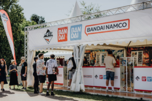 Ichiban Kuji Besucher stehen am Bandai Namco Stand auf dem Elbenwald Festival, um Merchandise und Informationen zu beliebten Anime- und Gaming-Produkten zu erhalten. Der Stand ist gut besucht und bietet eine Vielzahl an Ausstellungsstücken und interaktiven Elementen.