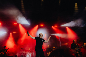 Bosse Ein Sänger auf der Bühne des Elbenwald Festivals, umgeben von roten Lichtern und Nebel, während Musiker im Hintergrund spielen. Die Atmosphäre ist lebhaft und energiegeladen, perfekt für Fans von Musik und geekiger Kultur.