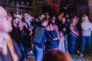 Paar tanzt fröhlich vor der Bühne beim Elbenwald Festival, umgeben von einer begeisterten Menge in bunten Outfits und Accessoires. Die Atmosphäre ist lebhaft und feierlich, während Musik und Gemeinschaft im Vordergrund stehen.