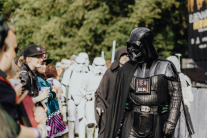 501st Legion Cosplay von Darth Vader und weiteren Charakteren aus dem Star Wars-Universum beim Elbenwald Festival. Die Szene zeigt begeisterte Fans in Kostümen und eine Gruppe von Stormtroopern im Hintergrund, die die nerdige Atmosphäre des Events unterstreichen.