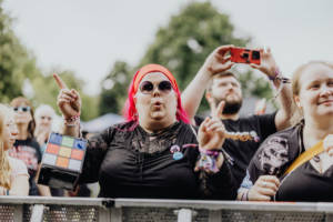 Festivalbesucher mit pinken Haaren und Sonnenbrille, die begeistert auf dem Elbenwald Festival mit einem Rubik's Cube in der Hand tanzen. Im Hintergrund sind weitere Teilnehmer zu sehen, die die Atmosphäre des Events genießen.