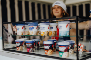 Scoops Ahoy Eisstände auf dem Elbenwald Festival bieten eine Auswahl an Scoops Ahoy-Eiscreme mit verschiedenen Geschmacksrichtungen. Im Hintergrund ist eine freundliche Verkäuferin zu sehen, die die Besucher mit kühlen Leckereien versorgt.