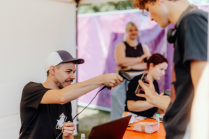 Ein Mitarbeiter scannt ein Ticket am Elbenwald Festival, während im Hintergrund weitere Festivalbesucher und Mitarbeiter zu sehen sind. Der Stand ist bunt dekoriert und vermittelt eine lebhafte Festivalatmosphäre.