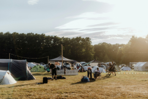 Zeltplatz beim Elbenwald Festival, mit zahlreichen bunten Zelten und Besuchern, die sich entspannen und die Atmosphäre genießen. Im Hintergrund sind Lichterketten und Bäume sichtbar, die die festliche Stimmung unterstreichen.