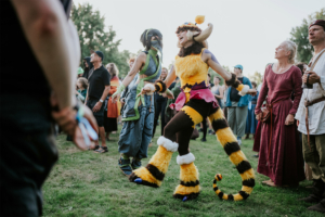 Zwei verkleidete Festivalbesucher tanzen begeistert auf dem Elbenwald Festival. Die bunte Kostümierung und die fröhliche Atmosphäre spiegeln die Verbindung von Musik und Fantasy wider, während die Menge im Hintergrund zuschaut.