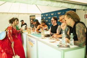 dArtagnan Besucher in Kostümen stehen an einem Tisch mit Künstlern beim Elbenwald Festival 2024. Die Szene zeigt eine lebhafte Interaktion zwischen Fans und Künstlern in einem festlichen Zelt voller Freude und Begeisterung.