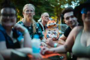 Menschen beim Elbenwald Festival, umgeben von bunten Plüschtieren und Merchandise. Die Atmosphäre ist entspannt und freundlich, während die Teilnehmer ihre Leidenschaft für die Nerdkultur teilen. Ein unvergessliches Erlebnis für Fans von Musik und Fantasie.