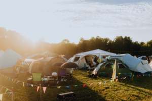Zelte und Campingstühle auf dem Elbenwald Festival, umgeben von bunten Wimpelketten. Die Abendsonne taucht die Szene in warmes Licht, während Festivalbesucher sich entspannen und die Atmosphäre genießen.