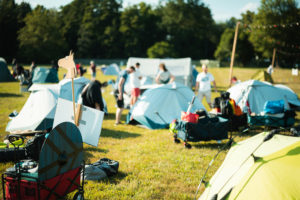 Zeltplatz beim Elbenwald Festival mit zahlreichen Zelten und Besuchern, die sich auf das Event vorbereiten. Im Vordergrund ist ein kreatives Schild in Form eines Pferdekopfes und ein Holzschild zu sehen, das die Atmosphäre des Festivals unterstreicht.