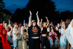 Eine fröhliche Menschenmenge beim Elbenwald Festival, die begeistert applaudiert und die Arme in die Höhe hebt. Die Szene zeigt eine vielfältige Gruppe von Festivalbesuchern, die gemeinsam die Musik und Atmosphäre genießen.