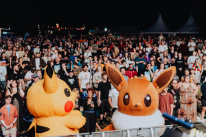 Zwei große, kostümierte Pokémon-Charaktere, Pikachu und Evoli, stehen vor einer begeisterten Menschenmenge bei einem Musikfestival. Die Atmosphäre ist lebhaft und zeigt die Verbindung von Musik und Nerd-Kultur auf dem Elbenwald Festival.