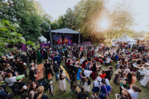 Corvus Corax Blick auf die Bühne des Elbenwald Festivals, umgeben von einer bunten Menge von Festivalbesuchern in kreativen Kostümen. Die Atmosphäre ist lebhaft, mit Musik und fröhlichen Gesichtern, die die einzigartige Mischung aus Musik und nerdiger Kultur feiern.