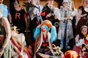 Cosplay Catwalk Bunte Cosplay-Gruppe auf dem Elbenwald Festival, mit einer Clownfigur im Vordergrund und anderen kreativen Kostümen im Hintergrund. Die Teilnehmer zeigen ihre Leidenschaft für Fantasy und Popkultur in einer lebhaften Festivalatmosphäre.