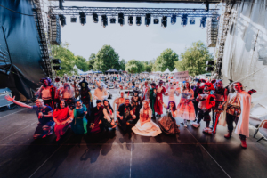 Cosplay Contest Bunt gekleidete Festivalbesucher posieren auf der Bühne des Elbenwald Festivals, umgeben von einer großen Menschenmenge im Hintergrund. Die Atmosphäre ist lebhaft und feierlich, mit einem Mix aus Musik und Kostümen, der die nerdige Gemeinschaft feiert.