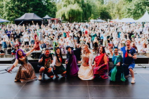 Cosplay Contest Bunt kostümierte Teilnehmer auf der Bühne des Elbenwald Festivals, umgeben von einer jubelnden Menge. Die Szene zeigt die lebendige Atmosphäre des Festivals, das Musik und Nerdkultur vereint.