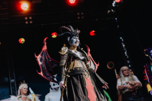 Cosplay Contest Cosplay auf der Bühne des Elbenwald Festivals: Eine charismatische Figur mit beeindruckendem Kostüm, geflügeltem Rücken und dramatischer Schminke, umgeben von weiteren Charakteren, die die kreative Vielfalt der Veranstaltung präsentieren.