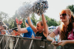 Cosplay Contest Ein begeistertes Publikum beim Elbenwald Festival, mit einem Mädchen, das Pompons hochhält, während andere Besucher applaudieren. Die Atmosphäre ist lebhaft und fröhlich, umgeben von einer bunten Menge und festlicher Stimmung.