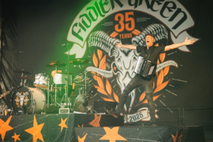 Fiddler's Green Ein Musiker von Fiddler's Green begeistert das Publikum beim Elbenwald Festival, während er auf der Bühne mit einem Akkordeon auftritt. Im Hintergrund ist das Festival-Logo und die Feierlichkeiten zum 35-jährigen Bestehen der Band zu sehen.