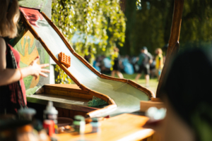 Eine kreative Waffelrutsche aus Holz auf dem Elbenwald Festival, umgeben von Besuchern. Die Rutsche dient als unterhaltsame Attraktion und zeigt das einzigartige, fantasievolle Ambiente des Festivals, das Musik und Nerdkultur verbindet.