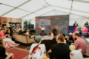 Gamesroom by Nerdistan Besucher des Elbenwald Festivals genießen ein Gaming-Event in einem Zelt, während sie auf großen Bildschirmen Mario Kart spielen. Die entspannte Atmosphäre wird von einer gemütlichen Sitzgelegenheit und nostalgischen Arcade-Spielen ergänzt.