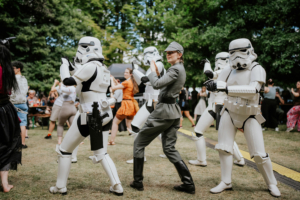 K-Pop-Dance Cosplay auf dem Elbenwald Festival: Eine Gruppe von Stormtroopers tanzt, während eine Person in militärischer Uniform im Vordergrund posiert. Die Szene spiegelt die kreative und lebendige Atmosphäre des Festivals wider, wo Fans ihre Leidenschaft für Popkultur feiern.
