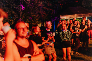 Buntes Publikum beim Elbenwald Festival, das eine lebendige Mischung aus Musik und nerdiger Kultur bietet. Festivalbesucher genießen die Atmosphäre, tragen Leuchtarmbänder und zeigen Begeisterung während einer Live-Darbietung unter bunten Lichtern.