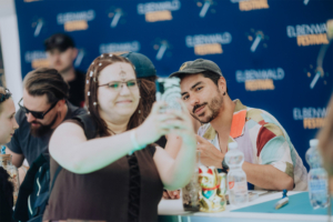 dArtagnan Ein Besucher des Elbenwald Festivals macht ein Selfie mit einem Teilnehmer, während andere Fans im Hintergrund warten. Die Szene zeigt die lebendige Atmosphäre des Festivals, das Musik und Nerd-Kultur vereint.