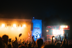 Nerds At Raves Bunt beleuchtete Bühne beim Elbenwald Festival 2026, umgeben von jubelnden Fans. Ein großes Banner mit dem Festival-Logo und eine LED-Leinwand, die "NERDS RAVE" zeigt, sorgen für eine lebendige Atmosphäre bei diesem einzigartigen Musik- und Nerd-Event.