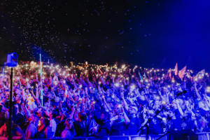 Ein begeistertes Publikum beim Elbenwald Festival hebt die Handys mit leuchtenden Bildschirmen in die Luft, während bunte Lichter und Seifenblasen die Nacht erhellen. Die Atmosphäre ist lebhaft und voller Energie, perfekt für Musik- und Nerdkultur-Fans.