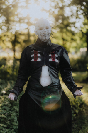 Ein kostümierter Teilnehmer des Elbenwald Festivals posiert in einem Wald. Die Person trägt ein auffälliges Outfit mit einer schwarzen Jacke und einer Maske mit Stacheln, umgeben von natürlicher Beleuchtung und grüner Umgebung.