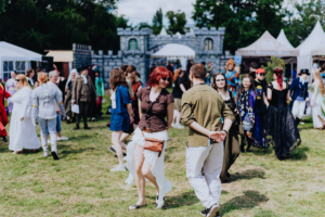 Historische Tänze Menschen in fantasievollen Kostümen tanzen und interagieren auf dem Elbenwald Festival, umgeben von Festzelten und einer mittelalterlichen Kulisse. Die lebendige Atmosphäre und die Vielfalt der Teilnehmer spiegeln die kreative Gemeinschaft wider.