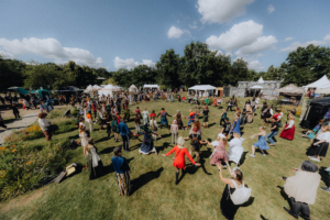 Historische Tänze Menschen in fantasievollen Kostümen tanzen im Freien auf dem Elbenwald Festival, umgeben von bunten Ständen und Zelten. Die Atmosphäre ist lebhaft und fröhlich, mit einer großen Menge, die gemeinsam eine unvergessliche Zeit erlebt.