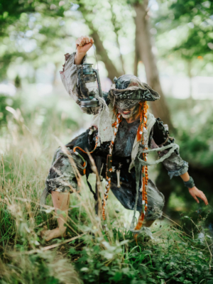 Ein verkleideter Festivalbesucher beim Elbenwald Festival, der mit einer Laterne in der Hand durch das Gras schreitet. Die kreative Kostümgestaltung zeigt einen fantasievollen Charakter, der zur einzigartigen Atmosphäre des Events beiträgt.
