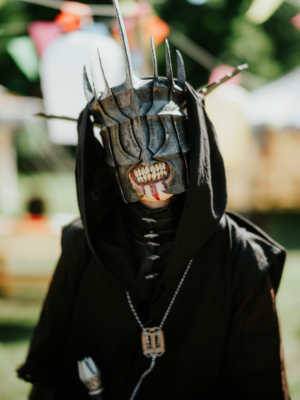 Ein Teilnehmer des Elbenwald Festivals trägt eine detaillierte Kostümmaske, die an einen fiktiven Charakter erinnert. Die Maske hat spitze Elemente und ein grinsendes Gesicht, das eine spannende Atmosphäre im Festivalgelände schafft.