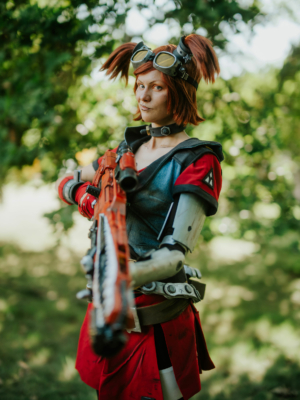 Cosplayer auf dem Elbenwald Festival, gekleidet in ein kreatives Outfit mit futuristischen Elementen und einer orangefarbenen Waffe, umgeben von grüner Natur. Der Charakter vermittelt ein Gefühl von Abenteuer und Fantasie, perfekt für das Festival.