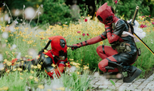Zwei Cosplayer im Deadpool-Kostüm interagieren in einem blühenden Garten beim Elbenwald Festival. Die Szene zeigt eine humorvolle und kreative Darstellung von Charakteren in einer lebhaften Umgebung voller Blumen.