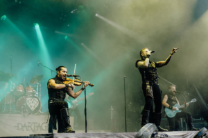 dArtagnan Auftritt der Band Dartagnan beim Elbenwald Festival, mit einem Violinisten und einem Sänger auf der Bühne, umgeben von Nebel und bunten Lichtern. Die energiegeladene Atmosphäre zieht das Publikum in ihren Bann und schafft ein einzigartiges Festivalerlebnis.
