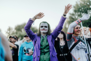 Ein Besucher im Joker-Kostüm hebt die Hände während des Elbenwald Festivals, umgeben von anderen kostümierten Fans. Die Atmosphäre ist lebhaft und feierlich, mit einer Mischung aus Musik und Cosplay.