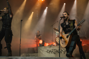 dArtagnan Auf der Bühne des Elbenwald Festivals performt die Band "Dartagnan" mit energiegeladenem Gesang und akustischer Gitarre. Die Lichtshow und die leidenschaftliche Atmosphäre schaffen ein mitreißendes Erlebnis für die Fans.
