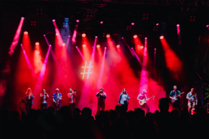 #zweiraumsilke Bühne beim Elbenwald Festival mit einer Band, die energetisch auftritt. Bunte Lichter und Nebel schaffen eine lebendige Atmosphäre, während das Publikum begeistert zuschaut. Ein unvergessliches Erlebnis für Musik- und Fantasy-Fans.